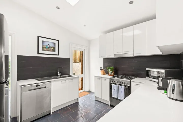 Una cocina moderna y luminosa con gabinetes blancos, salpicadero oscuro y electrodomésticos de acero inoxidable.