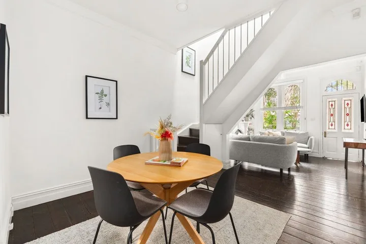 Un comedor da paso a una sala luminosa bajo una escalera.