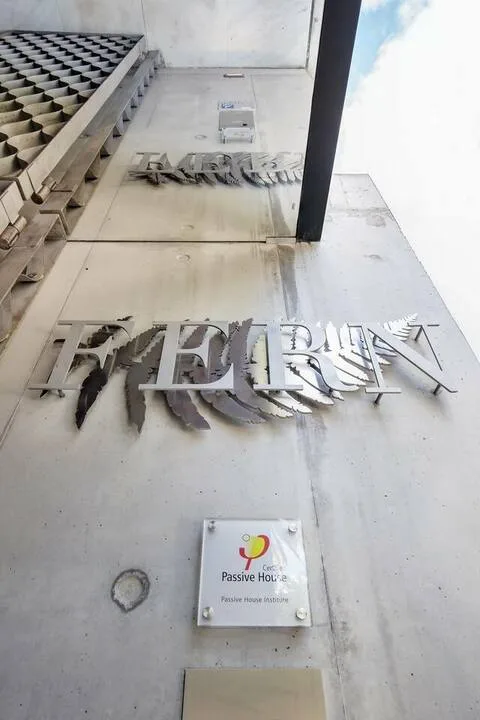 Vista hacia arriba de una fachada con letras en relieve y una placa pequeña.
