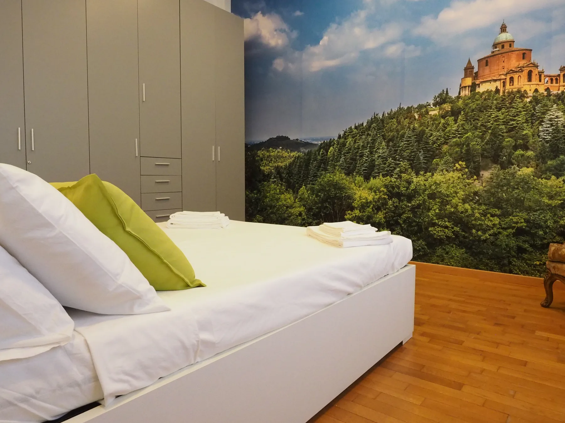 Un dormitorio con una cama blanca, almohadas verdes y un mural de bosque.