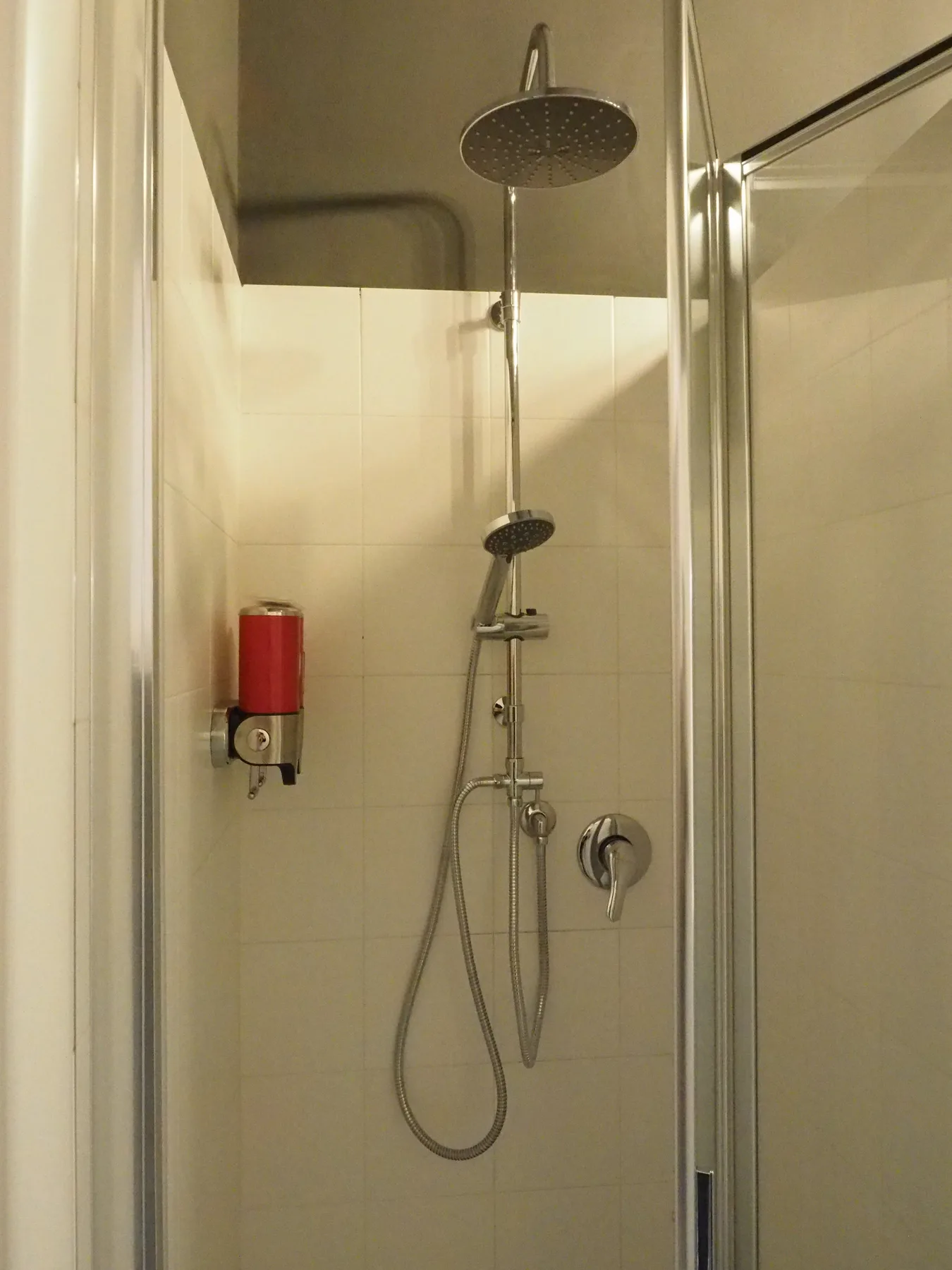 Una ducha con azulejos, un rociador superior grande y una ducha de mano.