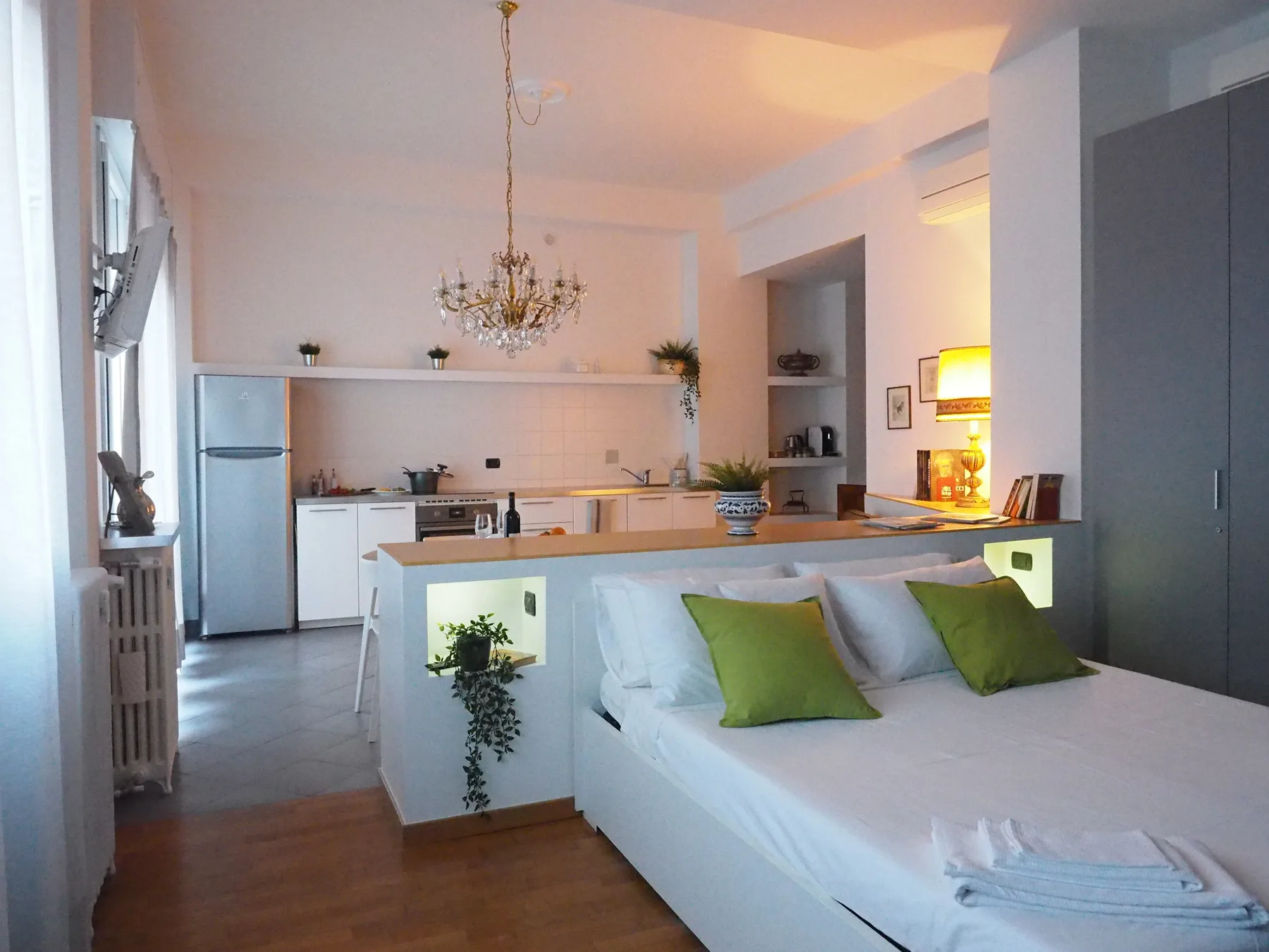 Una estancia diáfana y luminosa combina una cocina con una cama y cojines verdes.