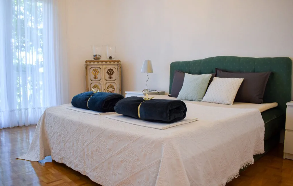 A bedroom with a large bed, green upholstered headboard, and tall curtained window.