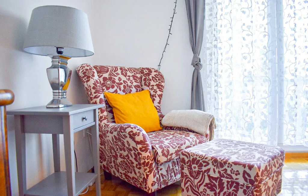 A patterned armchair and matching ottoman sit beside a window in a sitting area.