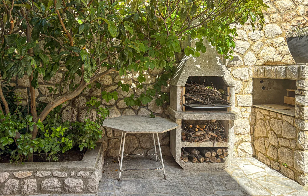 An outdoor stone cooking area with a wood-fired oven and a small table.