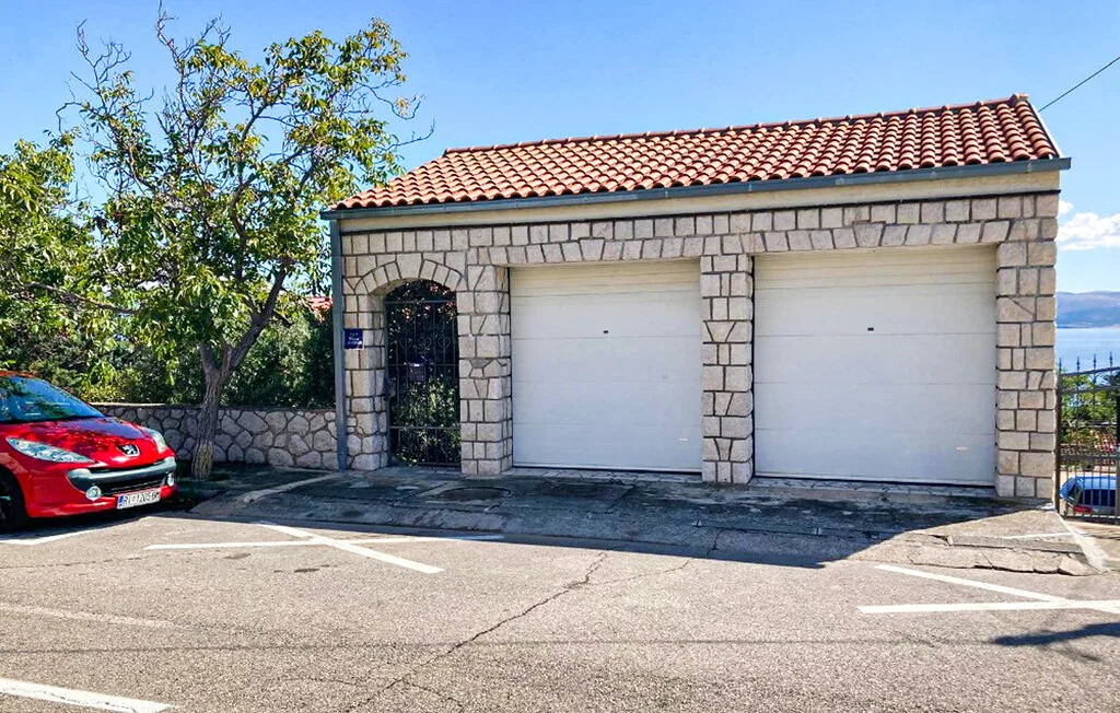 A roadside stone garage with two white doors and a red car parked nearby.