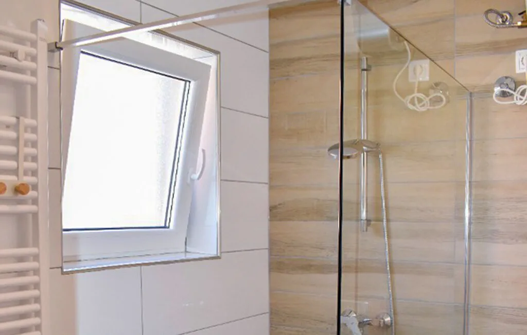 A bathroom with a glass shower and a slanted window.