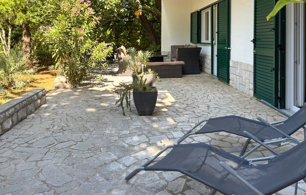 A stone-paved outdoor patio beside a white building, with lounge seating and potted plants.