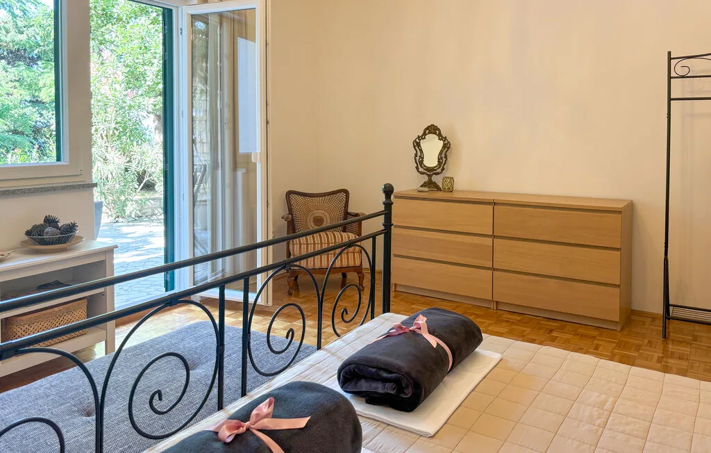 A bedroom with a metal bed frame, wooden dresser, and large windows.