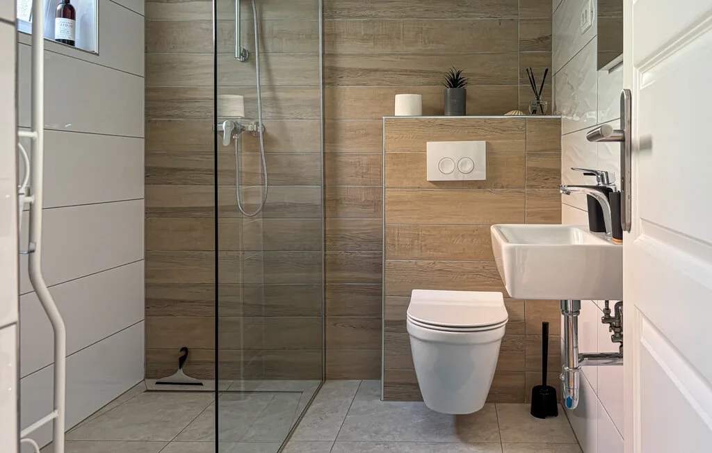 A modern bathroom with a glass shower, toilet, and wall-mounted sink.