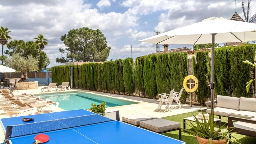 Una zona de piscina al aire libre con tumbonas, una sombrilla grande y una mesa de ping-pong.
