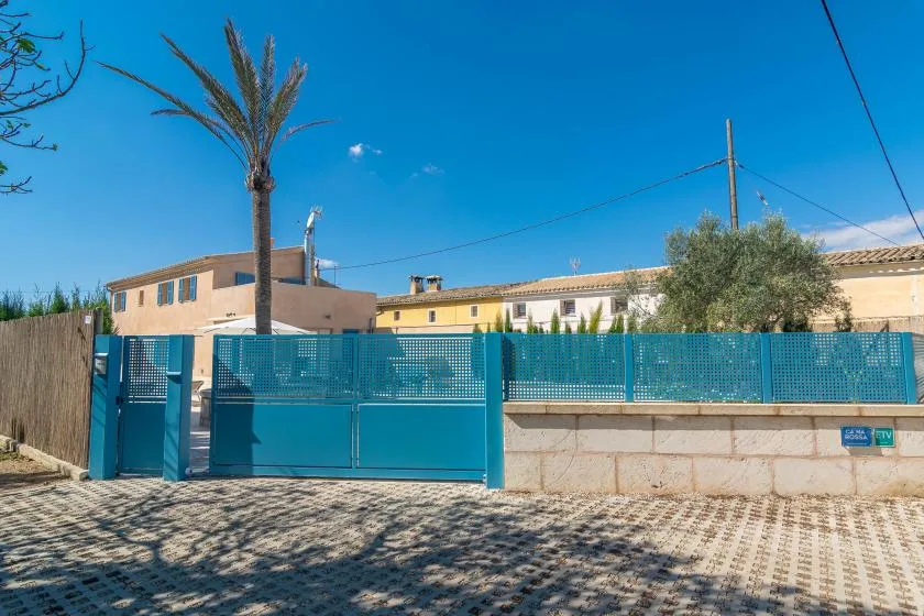 Una puerta metálica azul da a un muro bajo y edificios bajo un cielo despejado.