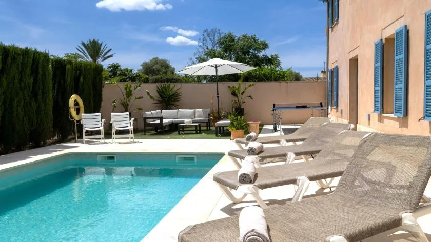 Un patio soleado junto a la piscina, con tumbonas y una sombrilla blanca.