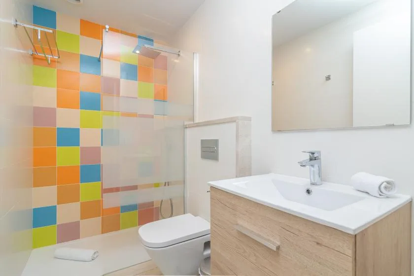 Un baño moderno con una ducha de azulejos coloridos y un mueble de lavabo en tonos de madera.