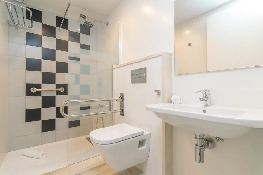 Un baño luminoso con ducha de azulejos, inodoro y lavabo de pared.