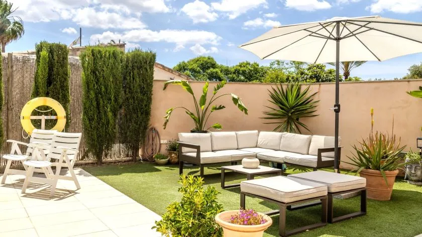 Un patio al aire libre con asientos acolchados, una mesa y una sombrilla grande.