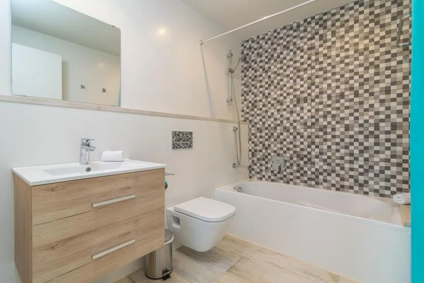Un baño con lavabo, inodoro y bañera junto a una pared de azulejos estampados.