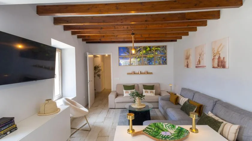Una sala de estar con asientos seccionales, mesa de centro y televisor en la pared.