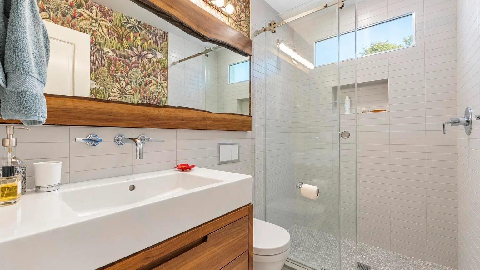 Un baño luminoso con un lavabo amplio, muebles de madera y una ducha de vidrio.