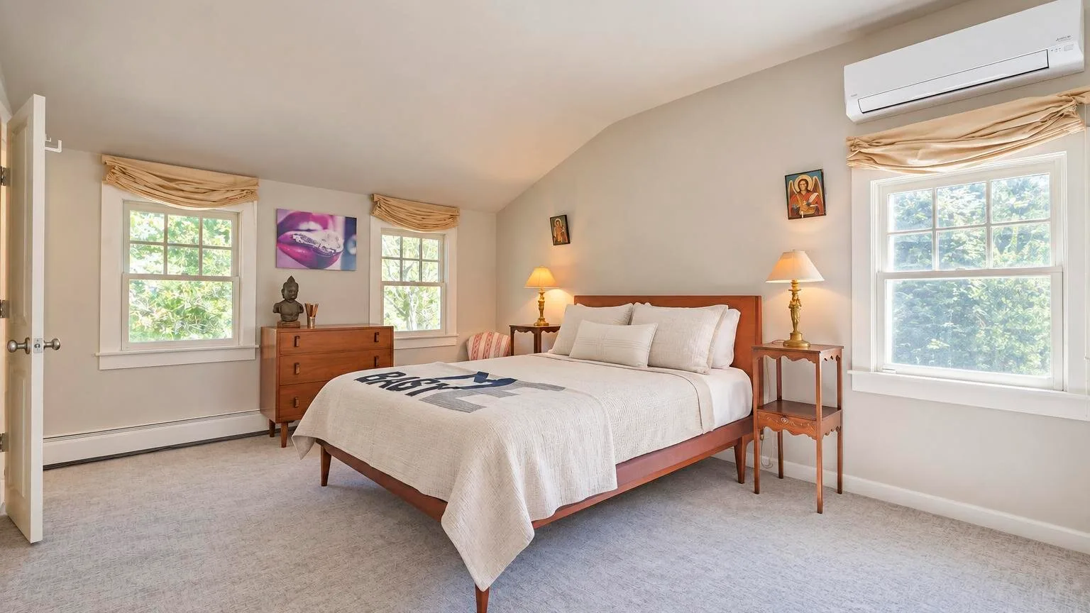 Un dormitorio luminoso con una cama grande, ventanas y mesitas de noche.