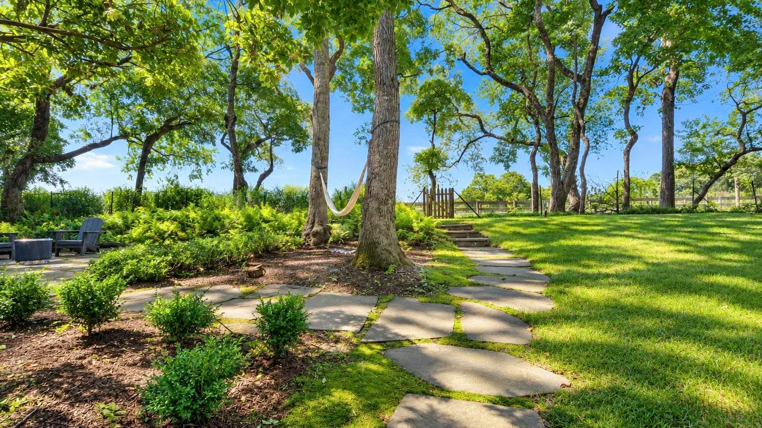 Un sendero sombreado atraviesa un jardín entre árboles, arbustos y césped.