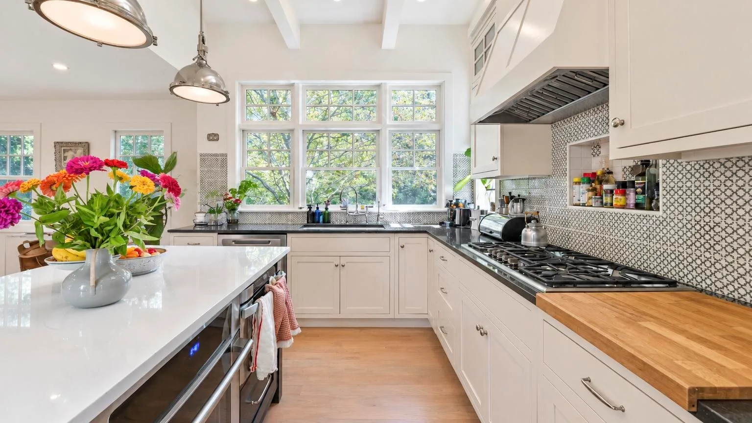 Una cocina luminosa con gabinetes blancos, una isla central y grandes ventanas.
