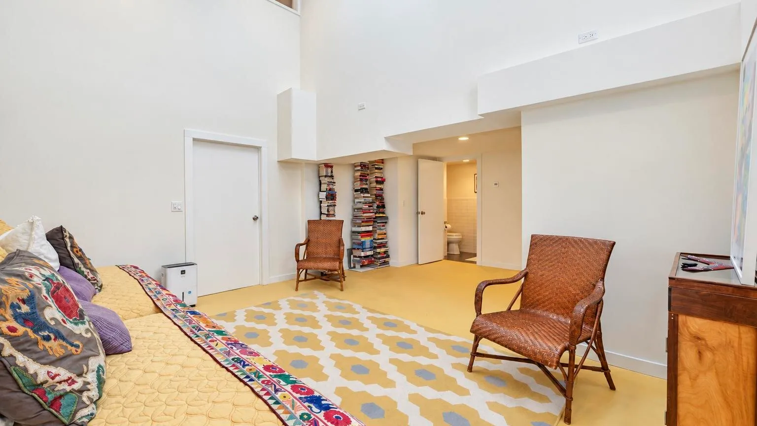 Una sala luminosa con cojines en el suelo, dos sillas y una alfombra estampada.