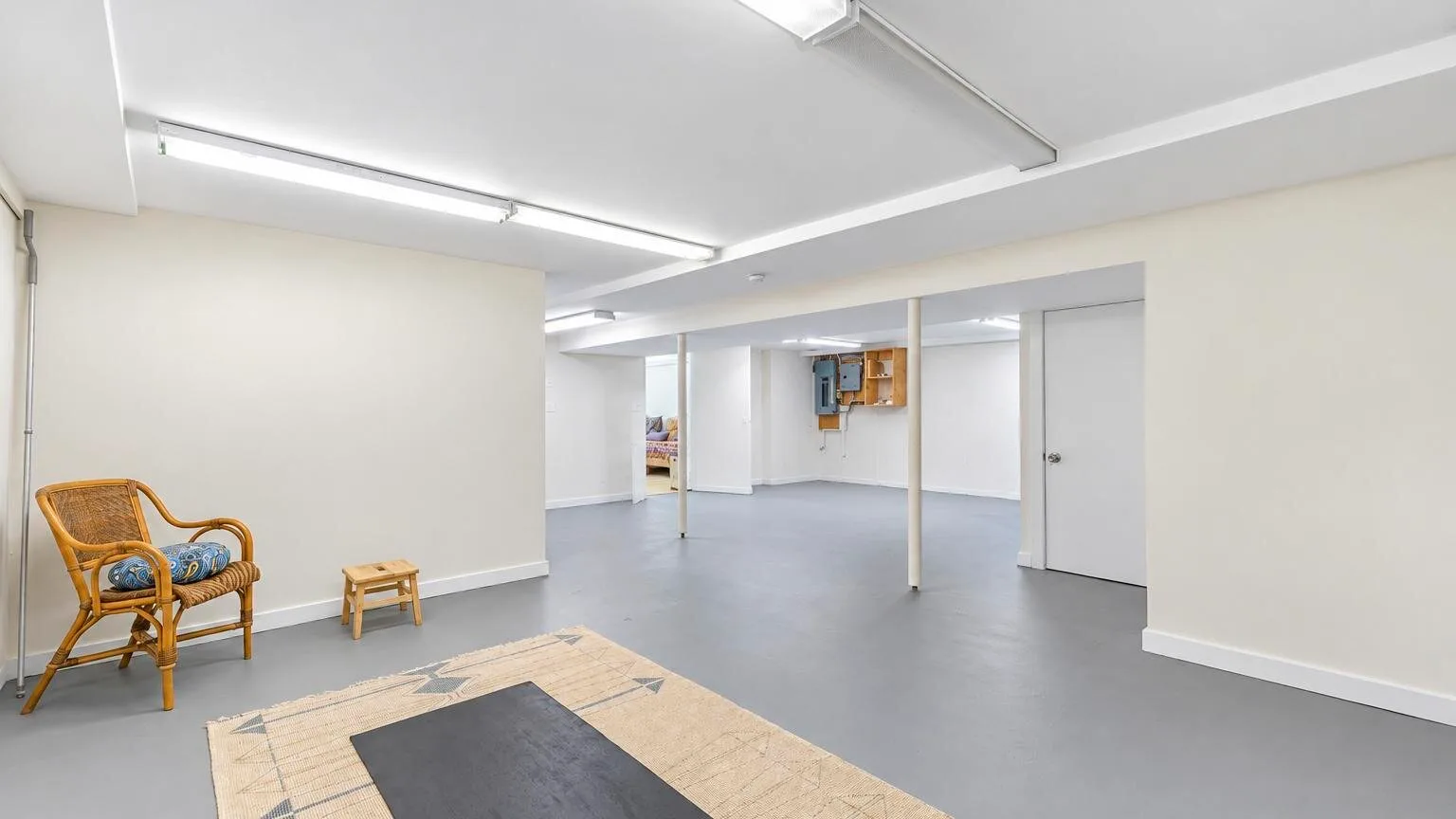 Una habitación amplia y luminosa con suelo gris y una zona de asientos de mimbre.