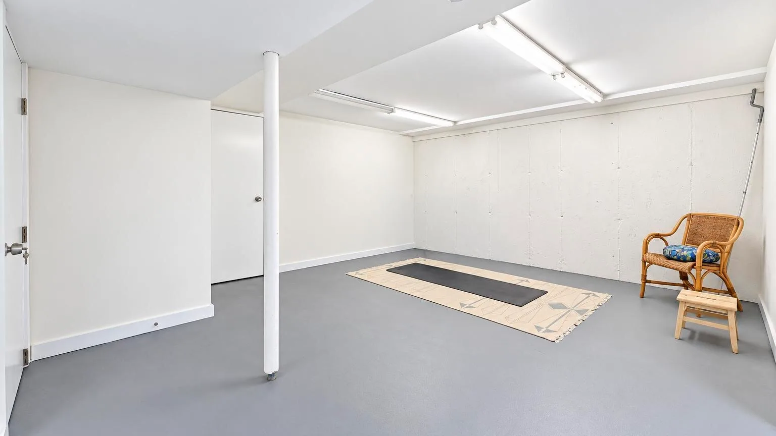 Una habitación vacía en el sótano con una esterilla y una silla de mimbre.