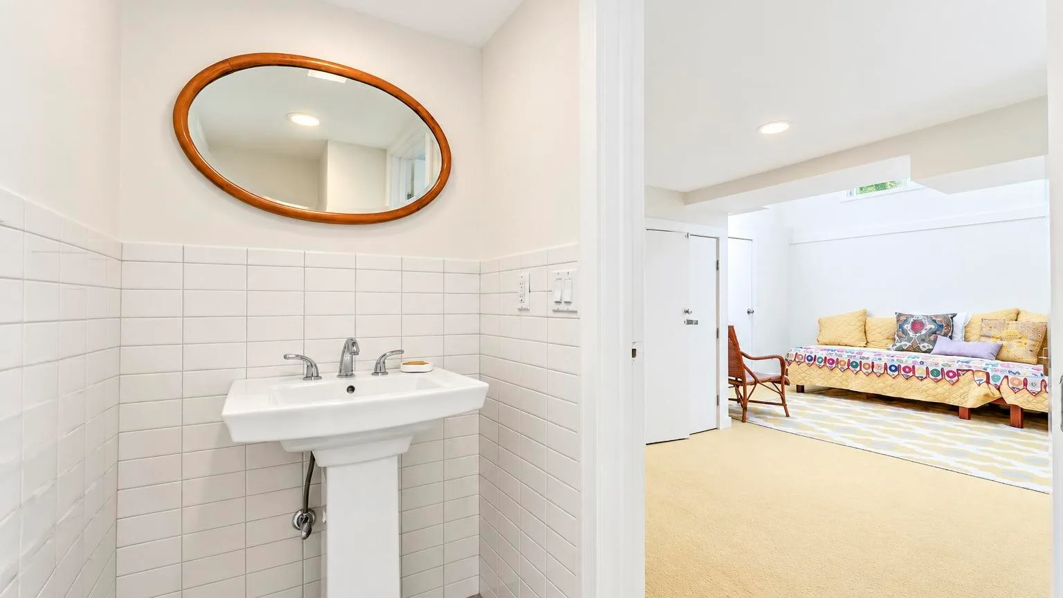 Un baño con azulejos y lavabo suspendido se abre a una luminosa sala de estar.