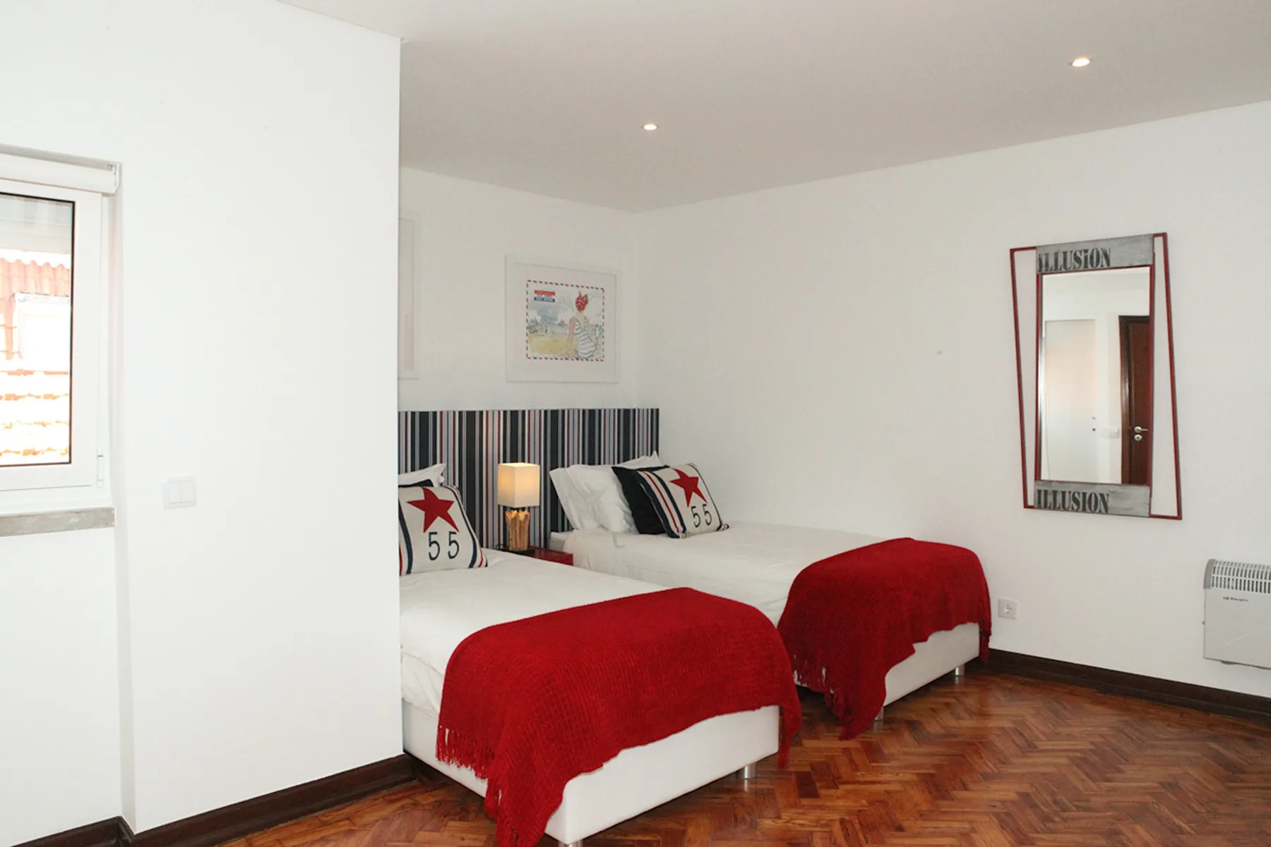 A bright bedroom with two beds dressed in red covers.
