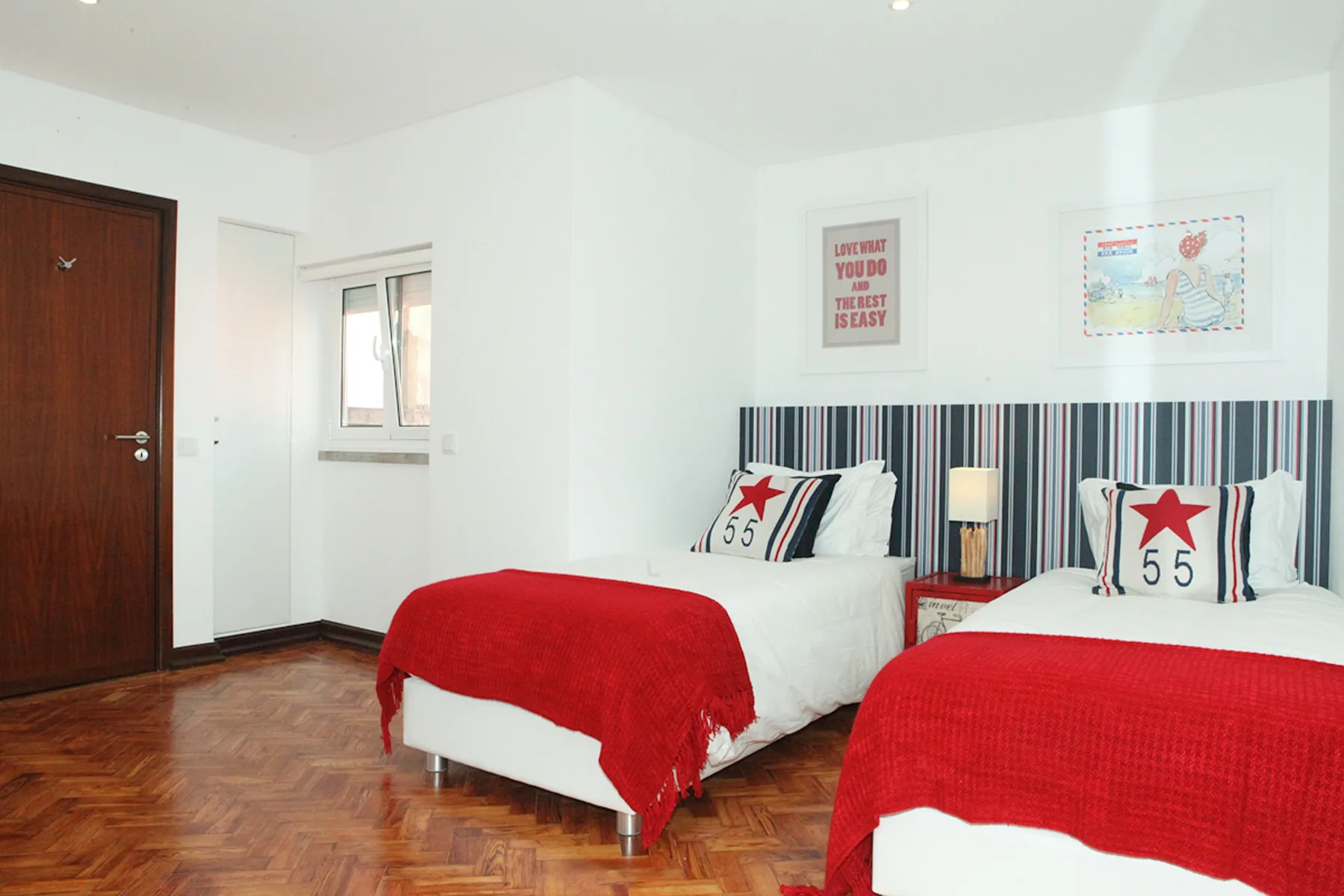A bright bedroom with two beds dressed in white and red bedding.
