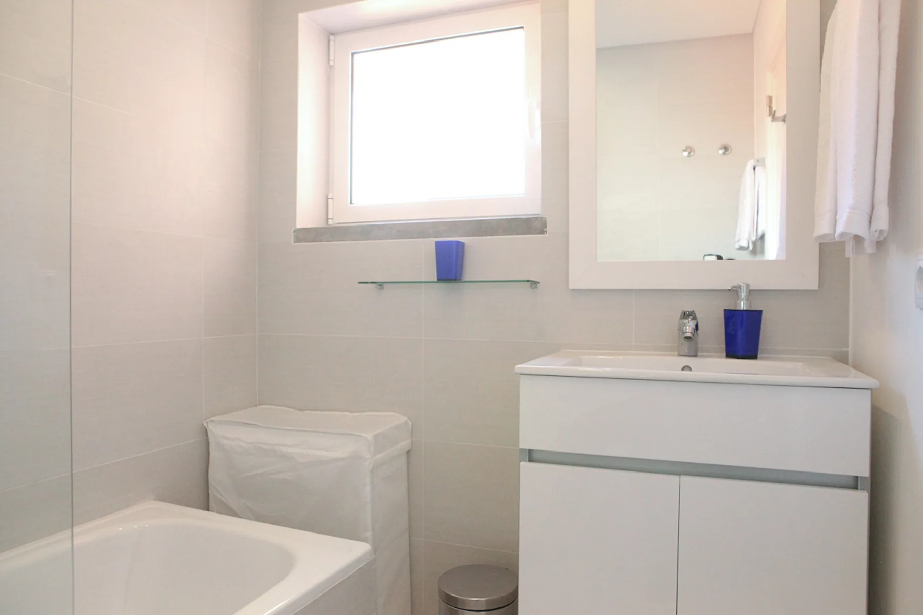 A bright bathroom with a sink, mirror, and bathtub.