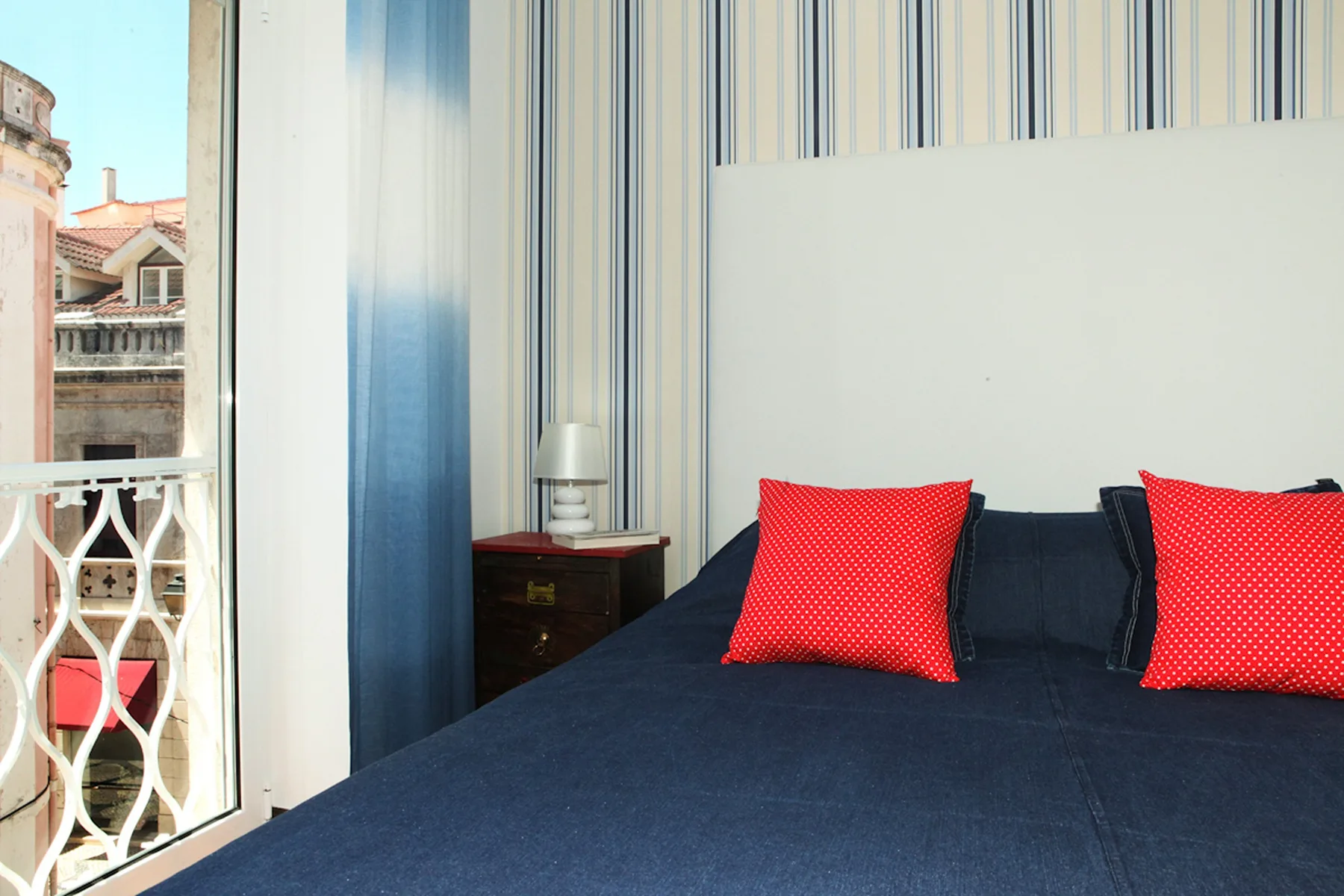A bedroom with a dark bedspread and red pillows beside a balcony door.