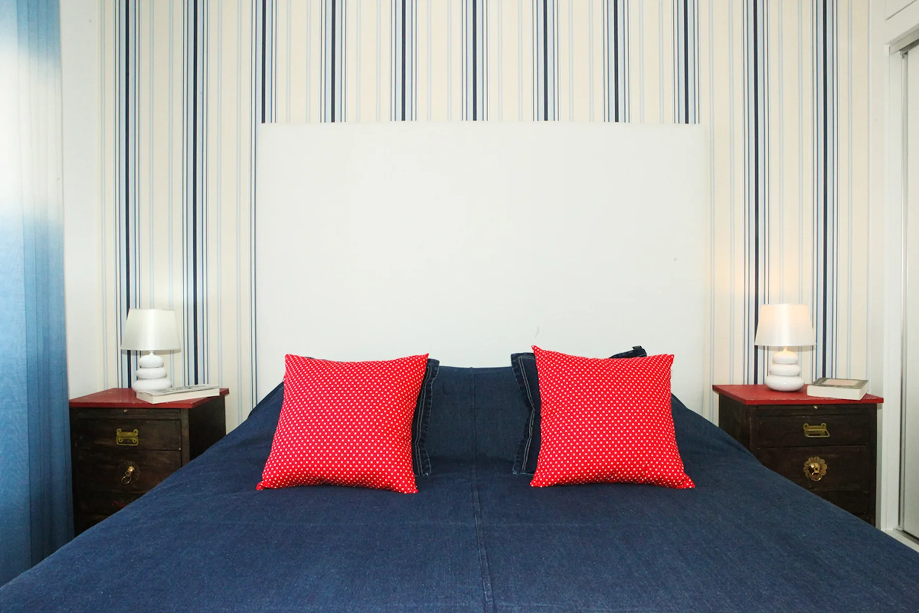 A bedroom with a dark bed, red pillows, and matching bedside tables.