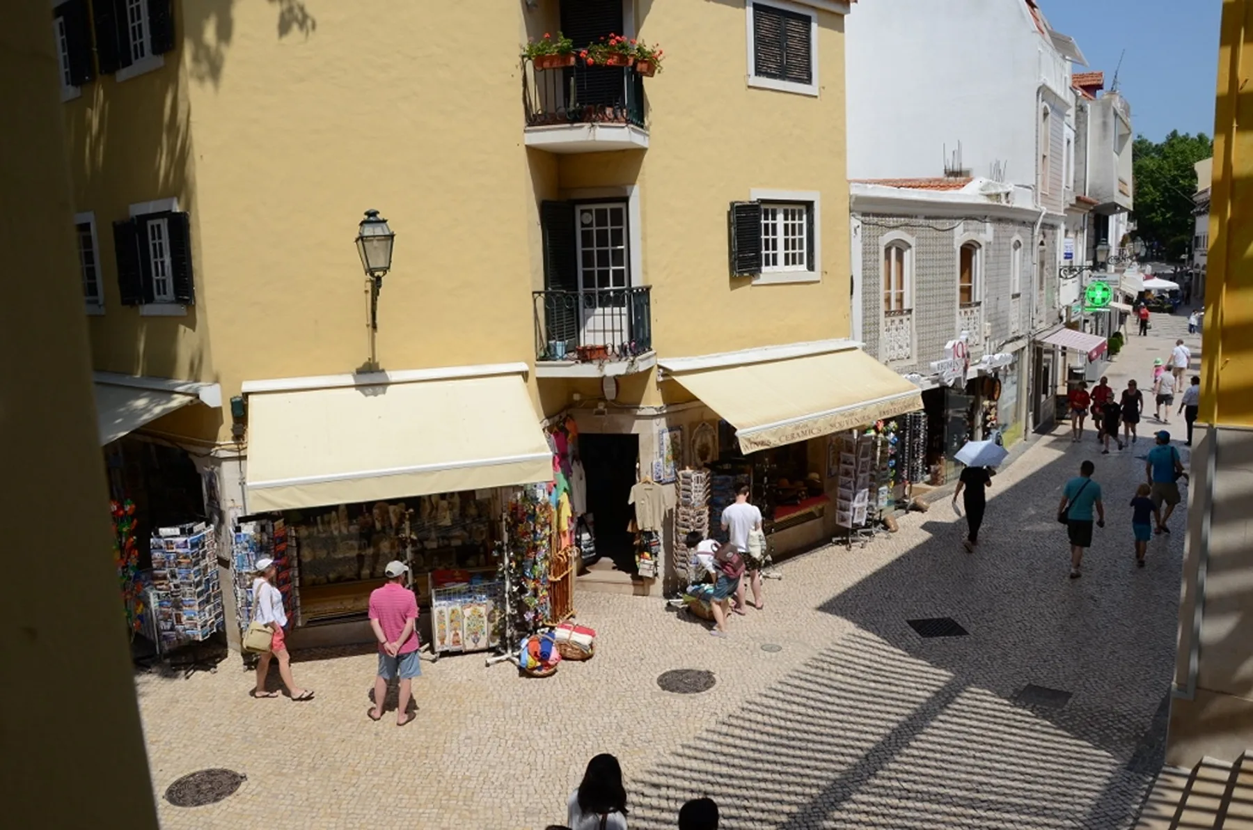 A sunny pedestrian street lined with shops and yellow and white buildings.