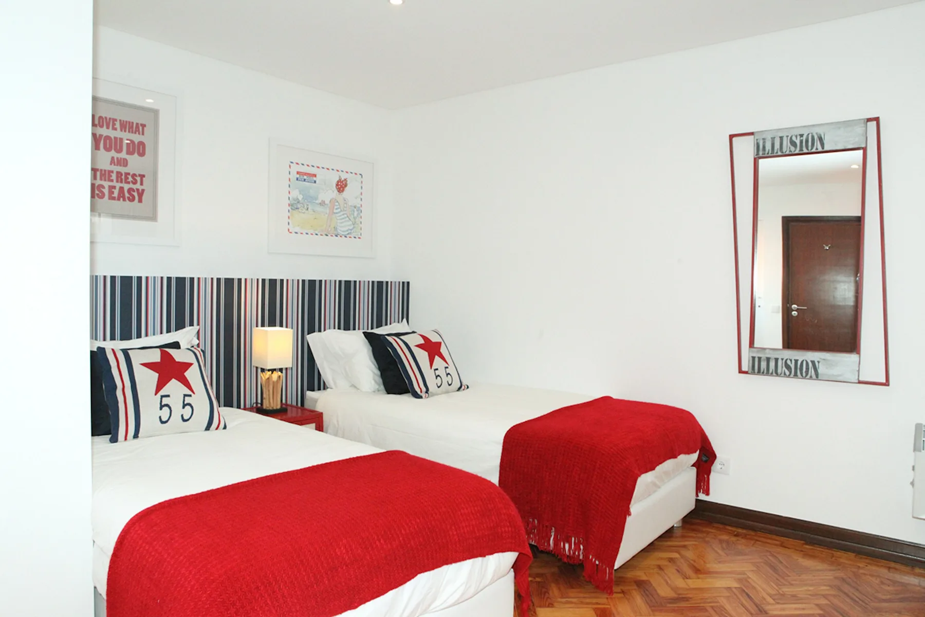 A bedroom with two beds, striped headboards, and red bed coverings.