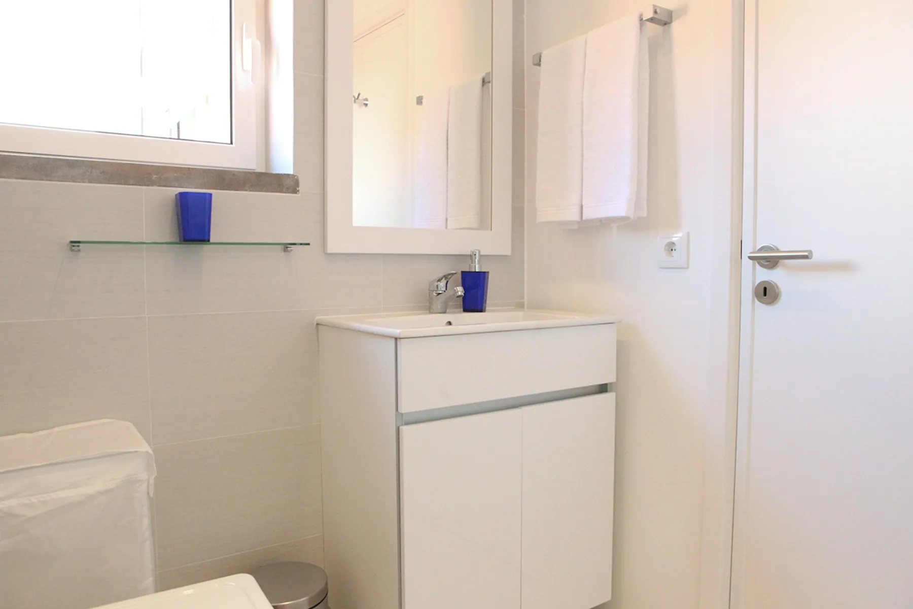 A bright bathroom with a sink vanity, mirror, and towel hanging on the wall.