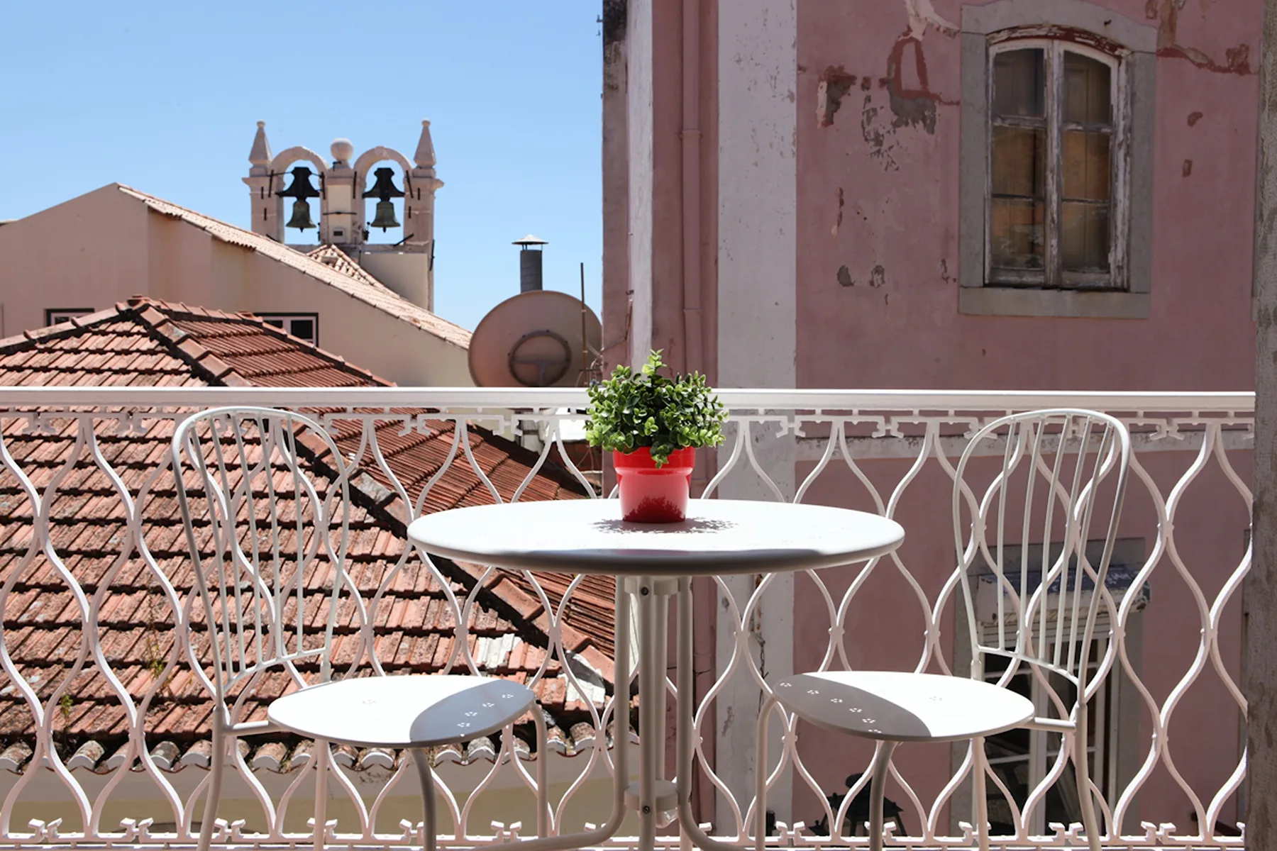 A small balcony with a round table and metal seating overlooks nearby rooftops.