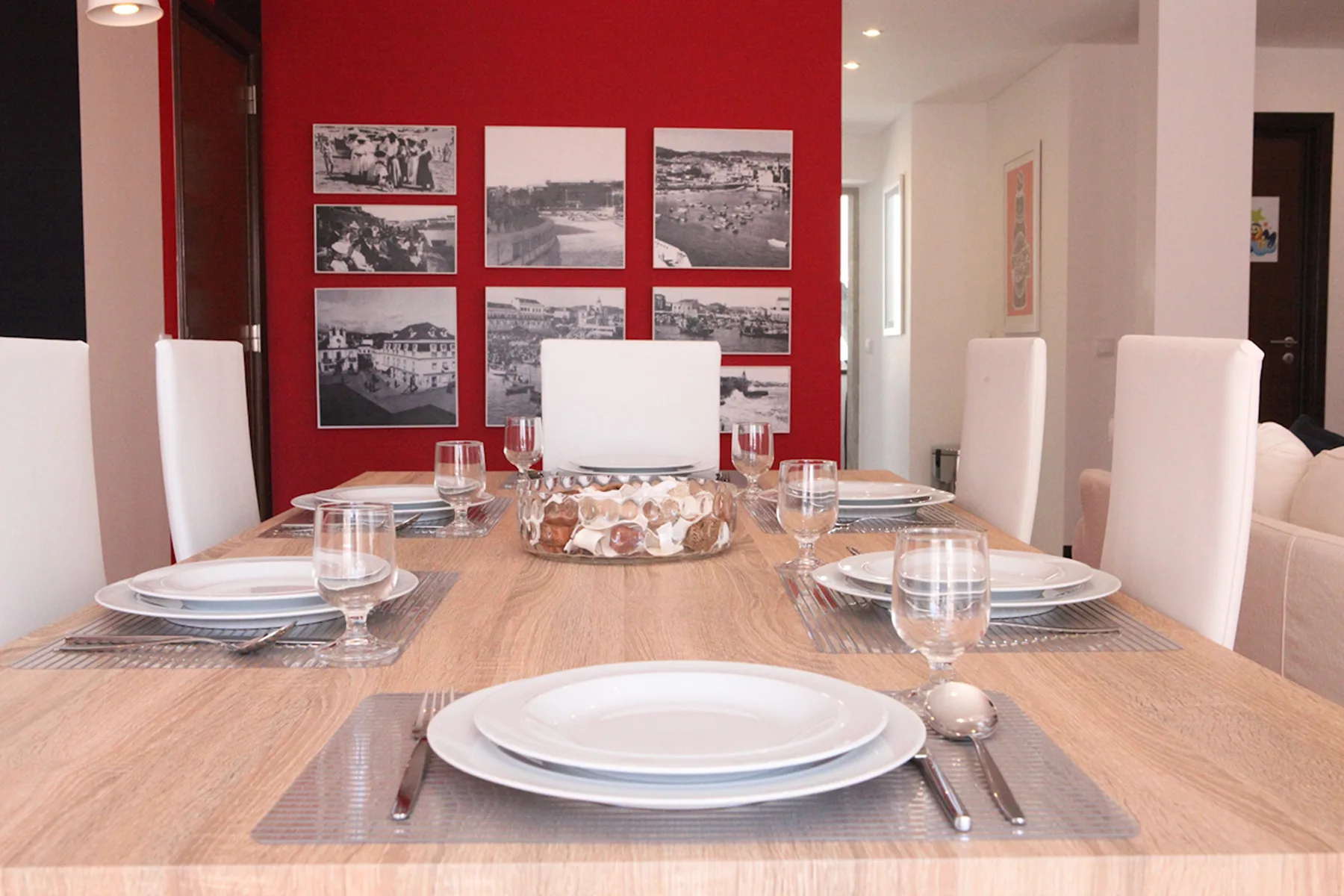 A dining room with a set table in front of a red wall with framed pictures.