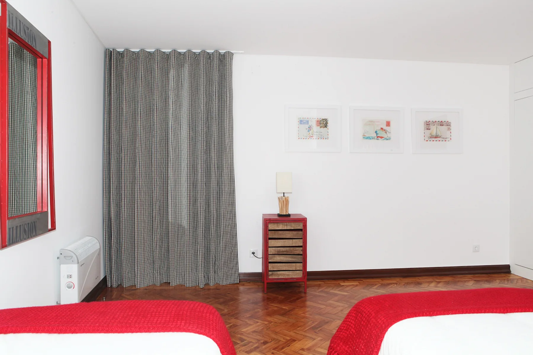 A bedroom with two beds, gray curtains, and framed artwork.