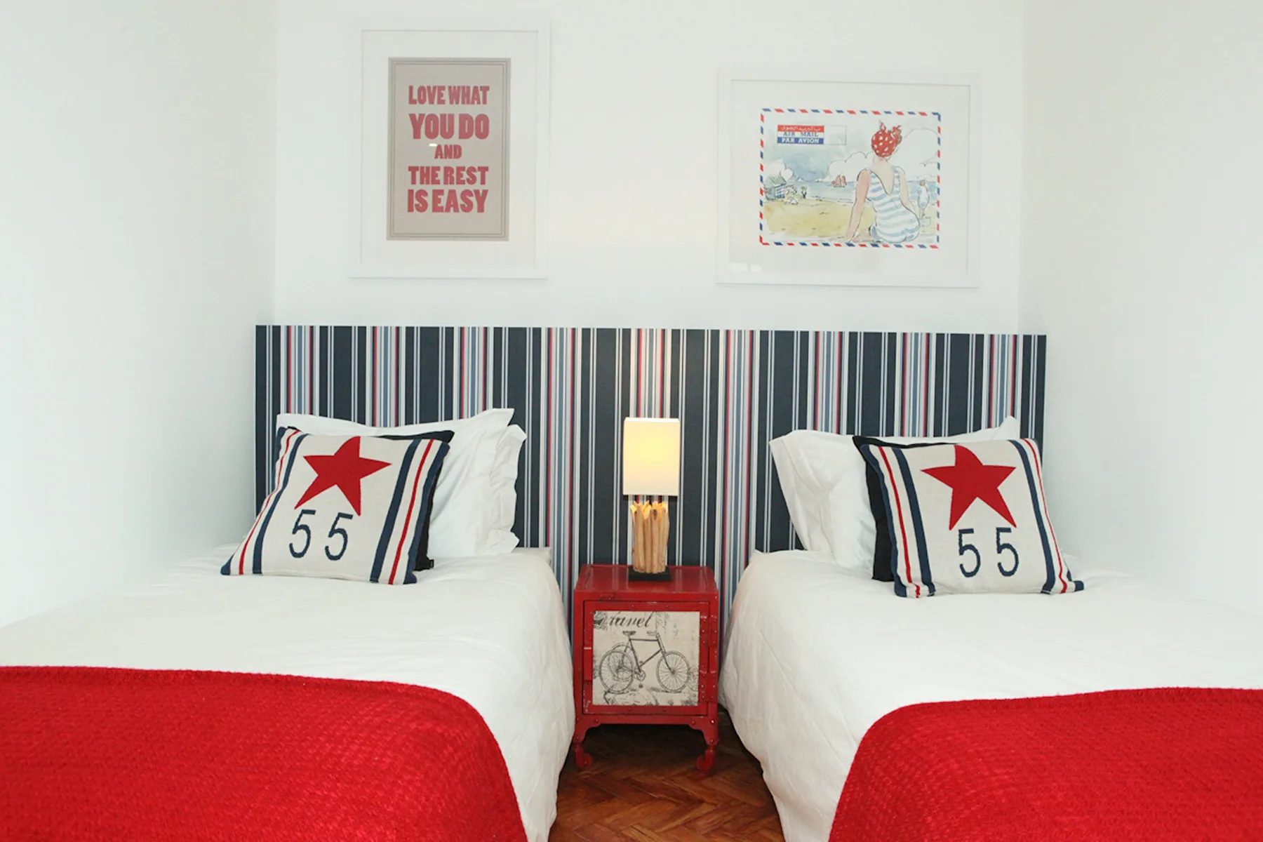 A bedroom with two beds, red bedspreads, and striped headboards.