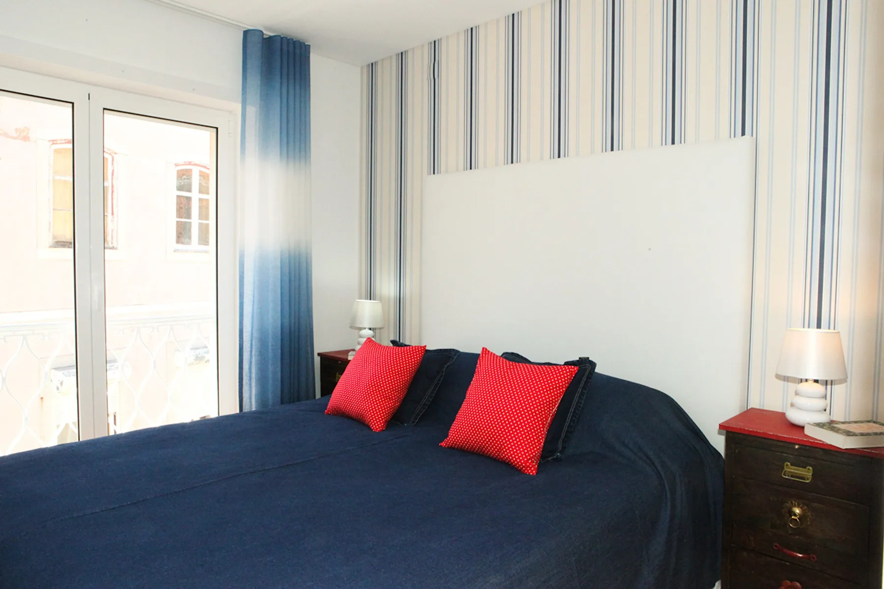 A bedroom with a dark bedspread, red pillows, and striped wallpaper.