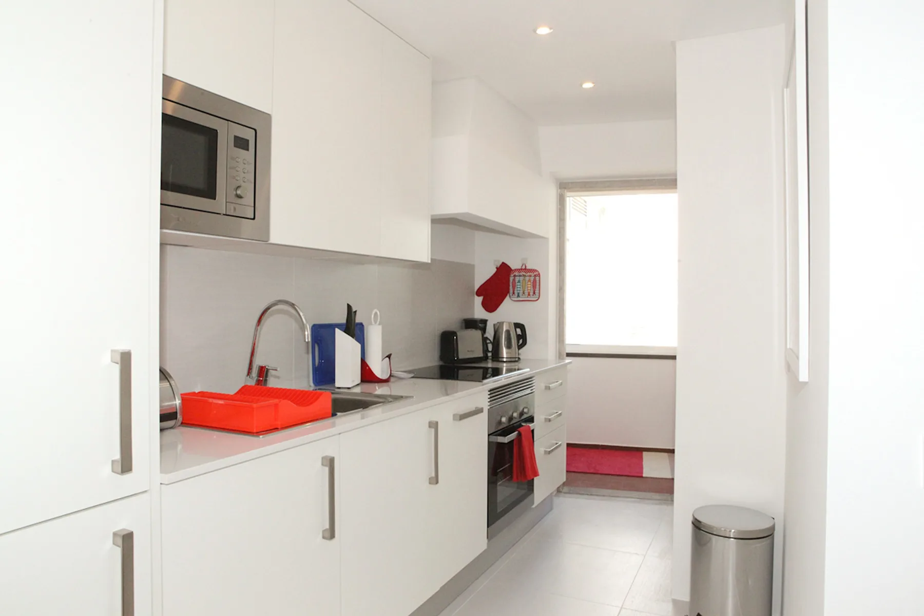 A bright white kitchen with a countertop, sink, and built-in appliances.