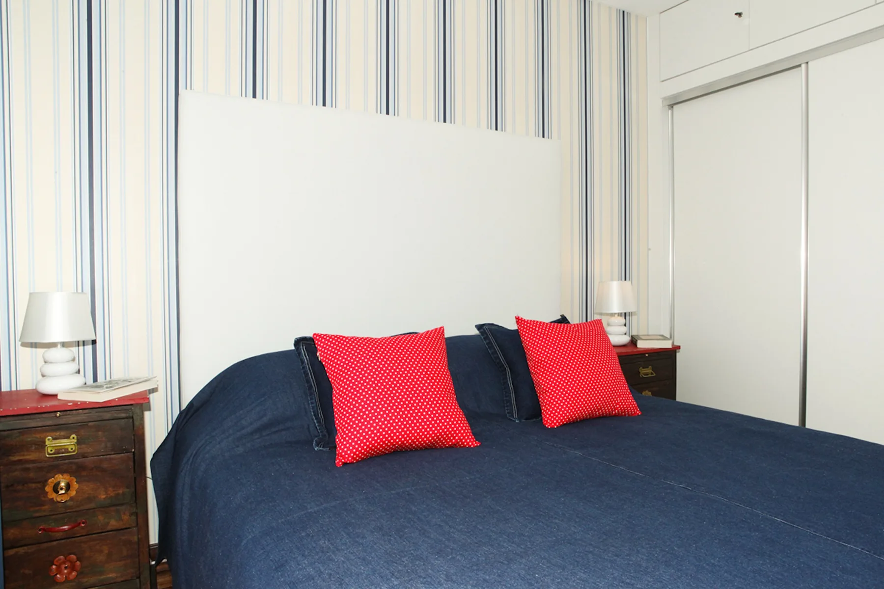 A bedroom with a dark bedspread and two bright red accent pillows.