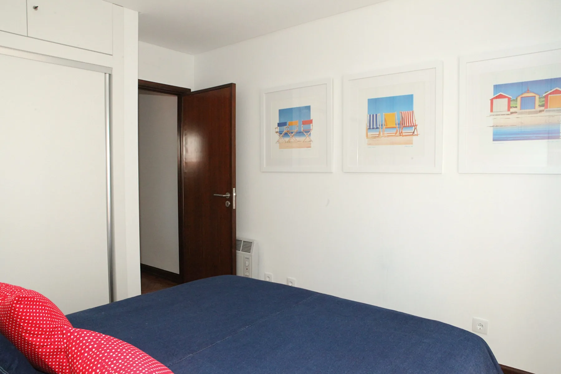 A bedroom with a blue bedspread and framed beach-themed artwork.