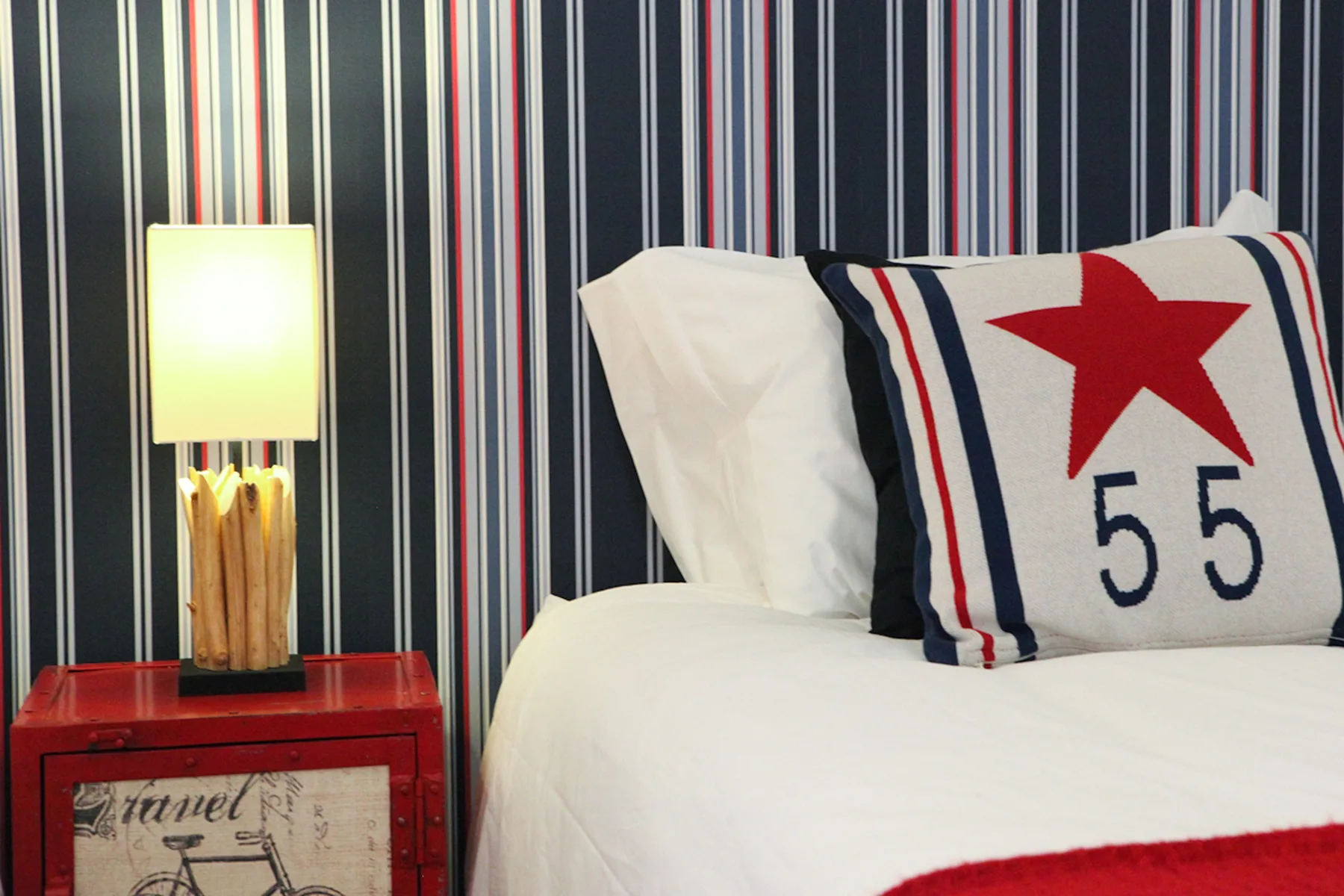 A bedroom with white bedding and a decorative pillow against striped wallpaper.