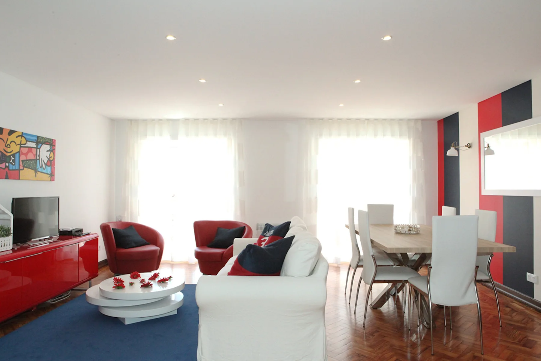 A bright living and dining room with seating, a television, and a dining table.