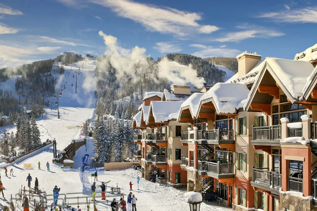 Edificios de un complejo cubiertos de nieve dan a una pista de esquí con esquiadores y telesillas.