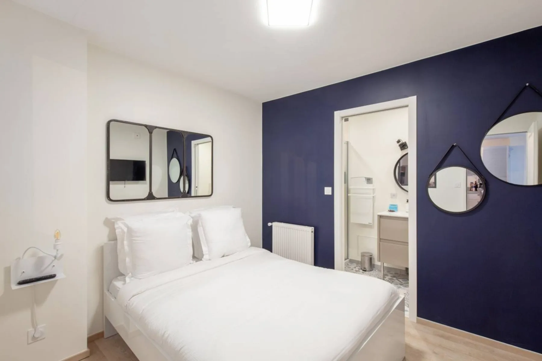 A bedroom with a neatly made bed and a dark blue accent wall.